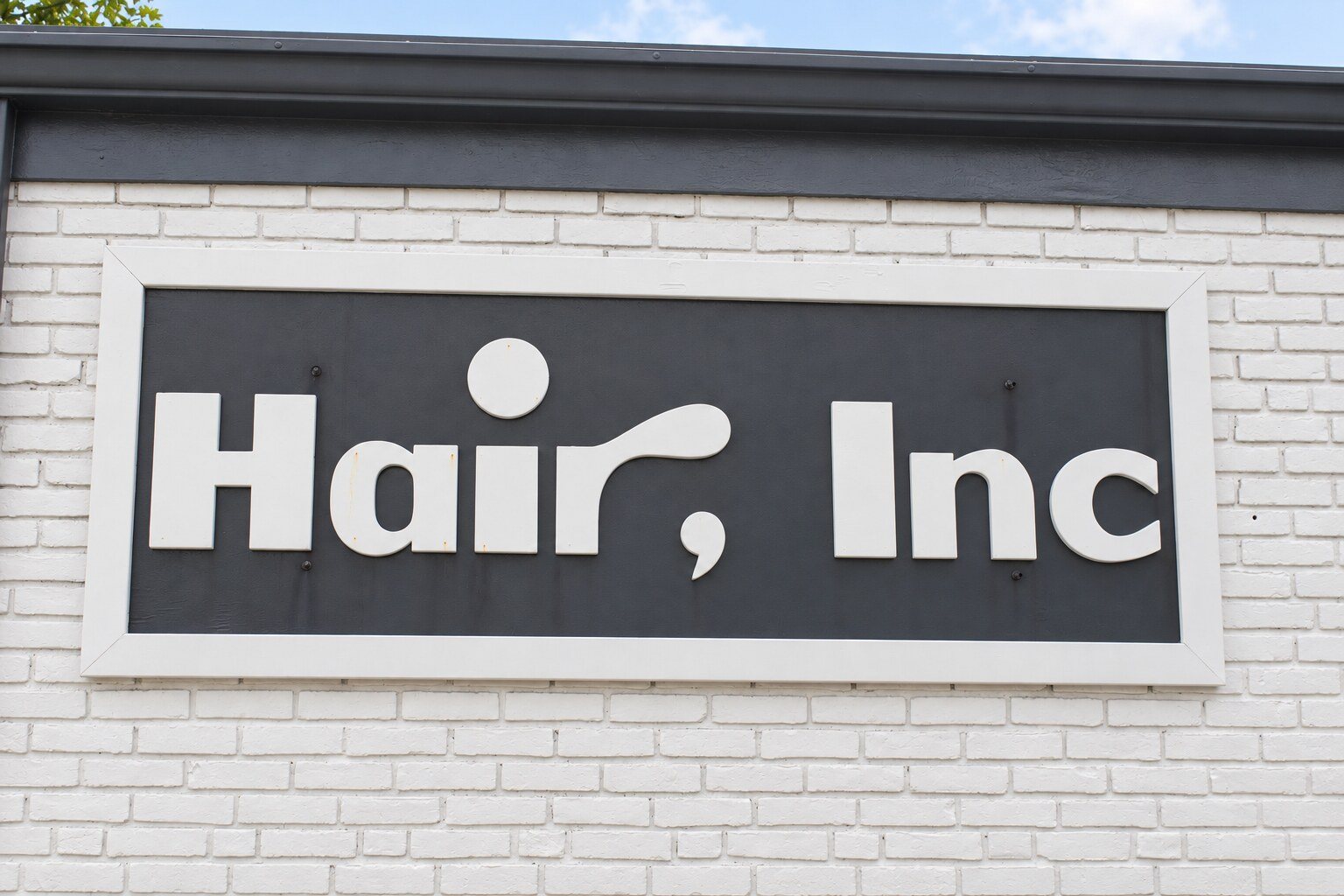 The Hair, Inc. sign on the white brick front of the salon